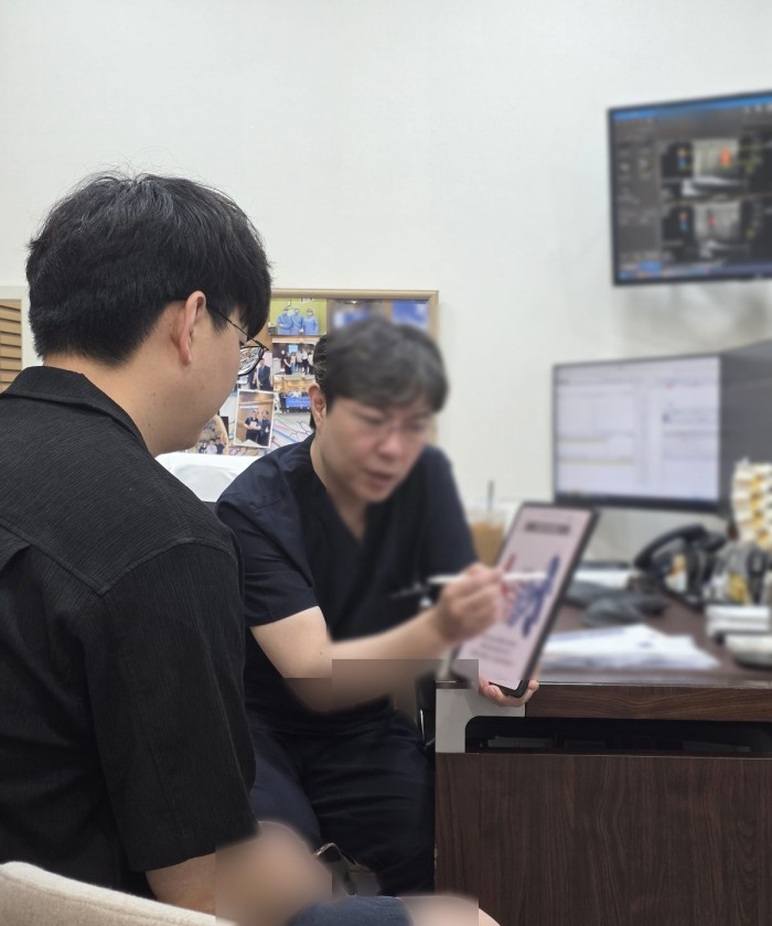 의료진이 진료실에서 태블릿을 보여 주며 환자에게 검사 결과를 설명하는 상담 장면.