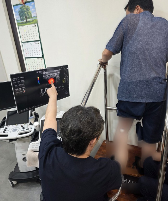 의료진이 초음파 장비로 서 있는 환자의 다리 혈관을 검사하는 모습.